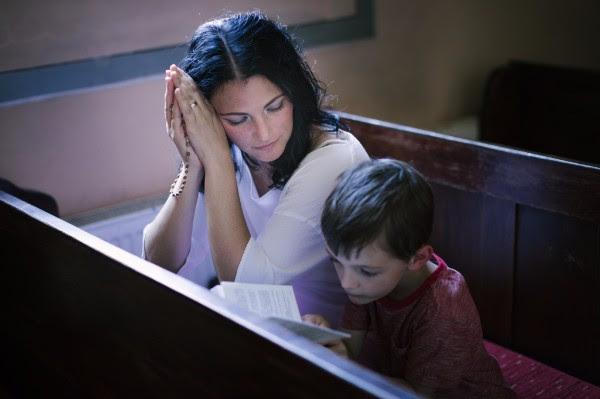 Mother praying with child in church.