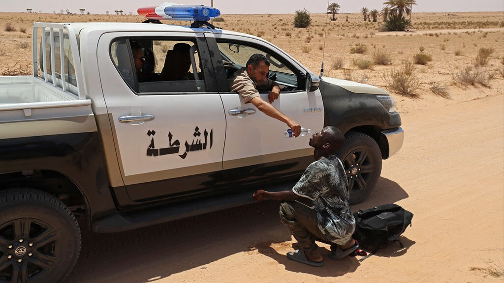 Een Libische grenswacht geeft water aan een man. De migrant is zonder water en voedsel achtergelaten in een woestijngebied.