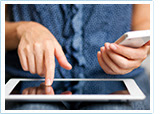 una mujer trabaja en un tablet mientras sostiene un teléfono móvil