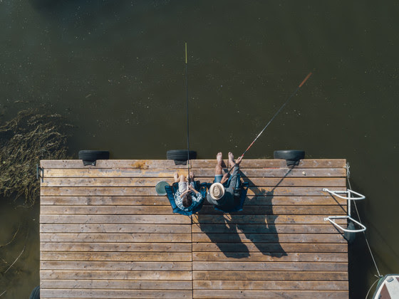 A photo taken from above of two people sitting at the end of a wooden pier fishing.