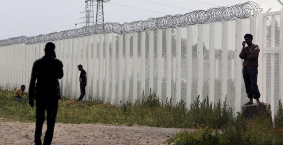 Varios inmigrantes llaman por teléfono cerca de una cerca con alambre de púas, junto al campamento improvisado llamado "La nueva jungla" en Calais, Francia.- REUTERS / Regis Duvignau