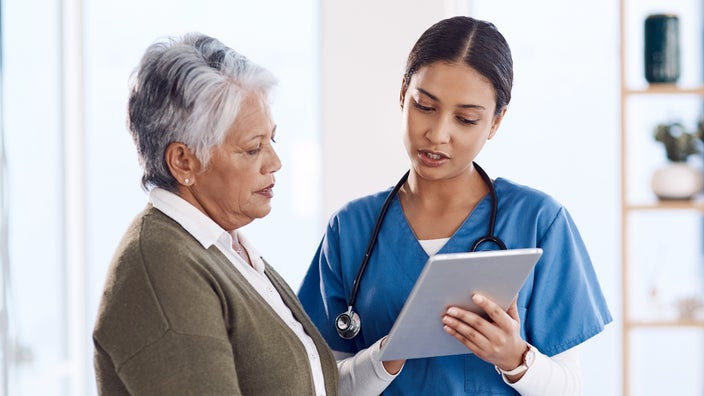 A woman and a nurse are reviewing test results on a tablet device.