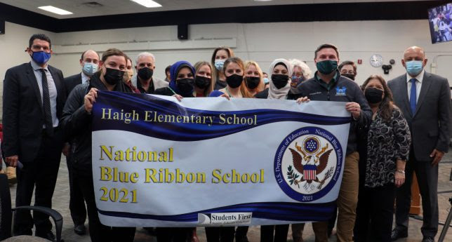 A group of school staff and district officials pose with a sign celebrating Haigh Elementary receiving a 2021 National Blue Ribbon School Award.