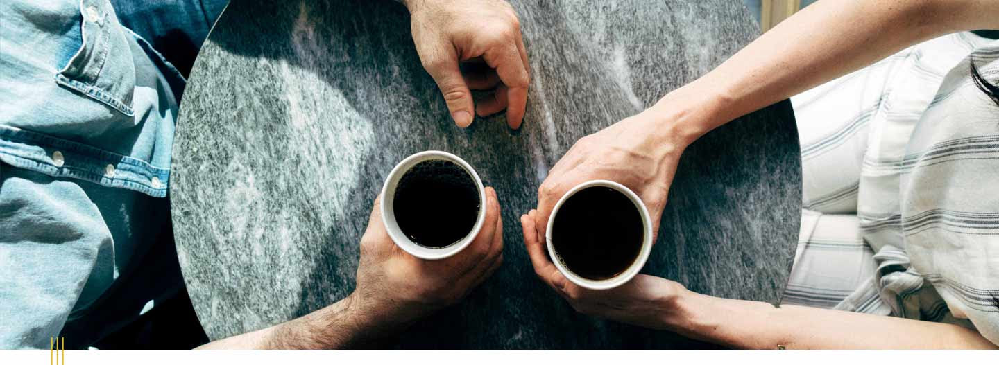 Top-down view of two cups of coffee being held by hands on a marbled tabletop