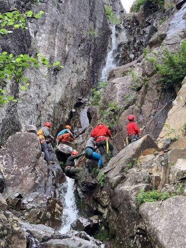 Forest Rangers and hikers using ropes to climb down rock wall