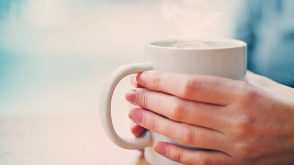 a person holding a mug of hot water that they are going to sip because that is how to stop a coughing attack