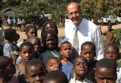Roger Glass poses outdoors with a group of African children