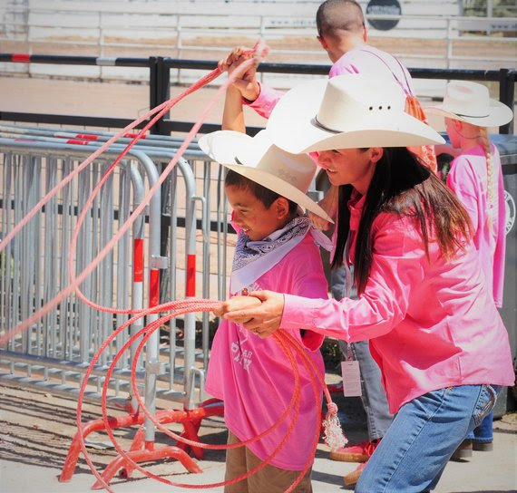 Dressed in pink shirts and cowboy hats, a teacher helps an elementary student learn how to rope at the Challenge Rodeo.