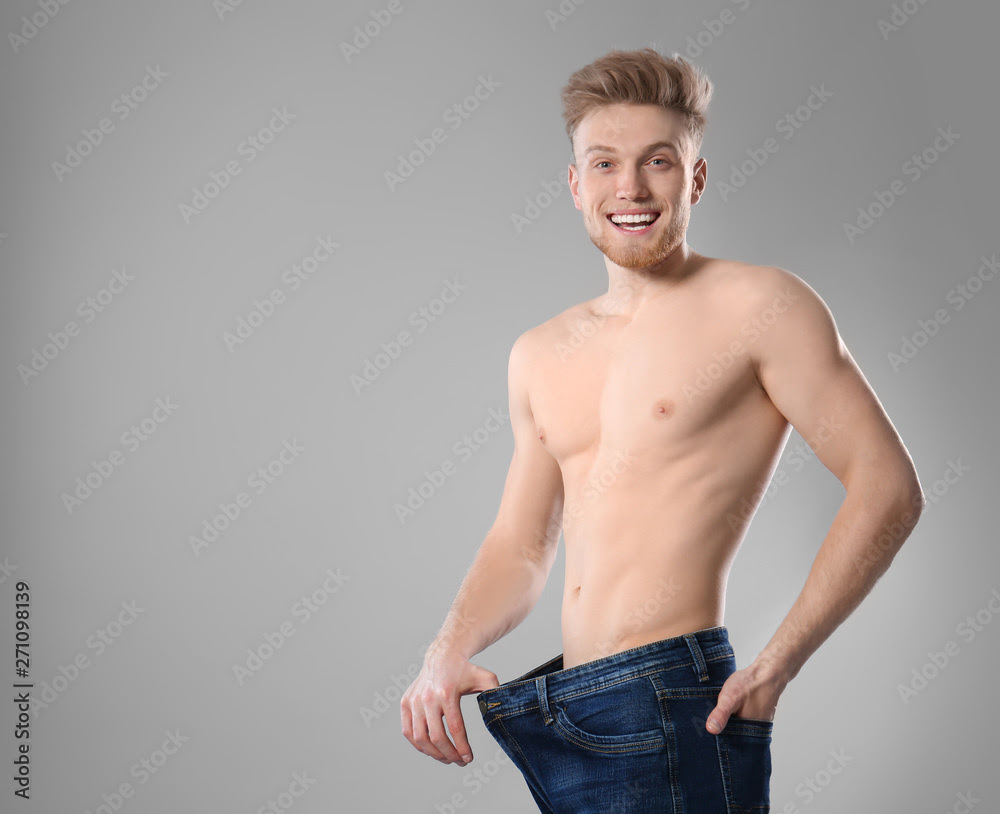 Young man with slim body in old big size jeans on grey background. Space  for text Stock Photo | Adobe Stock