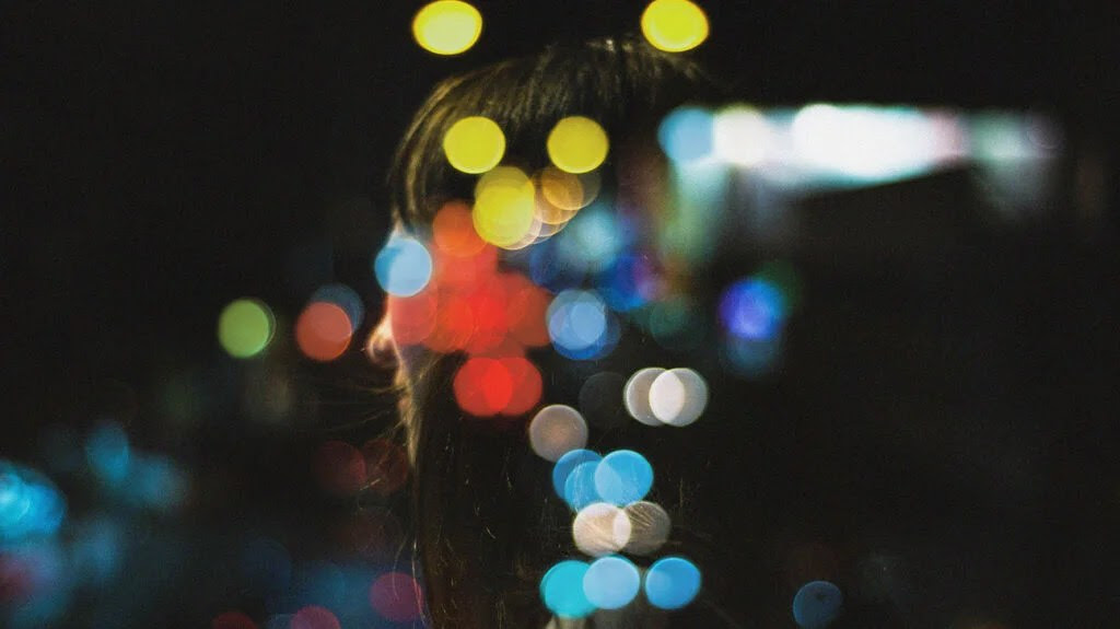 Dots of light in red, blue, and yellow, partially obscuring the image of a woman to represent migraine aura.