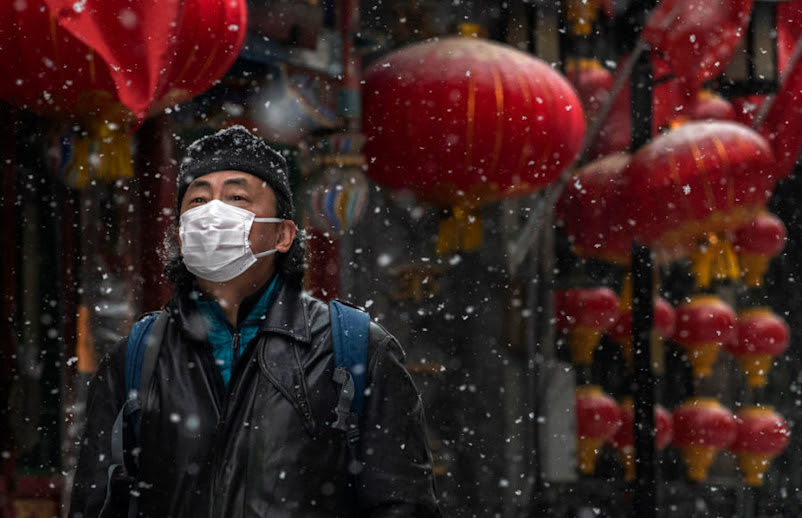 Un hombre chino usa una máscara protectora mientras camina durante una nevada en una calle comercial vacía y cerrada el 5 de febrero de 2020 en Beijing, China.
