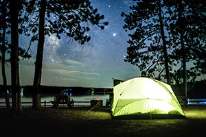 tent on wooded campsite by lake at night