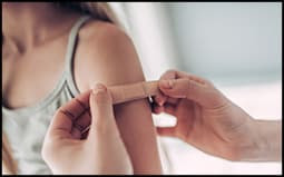 The figure shows a girl receiving an adhesive bandage on her upper arm from her pediatrician. 