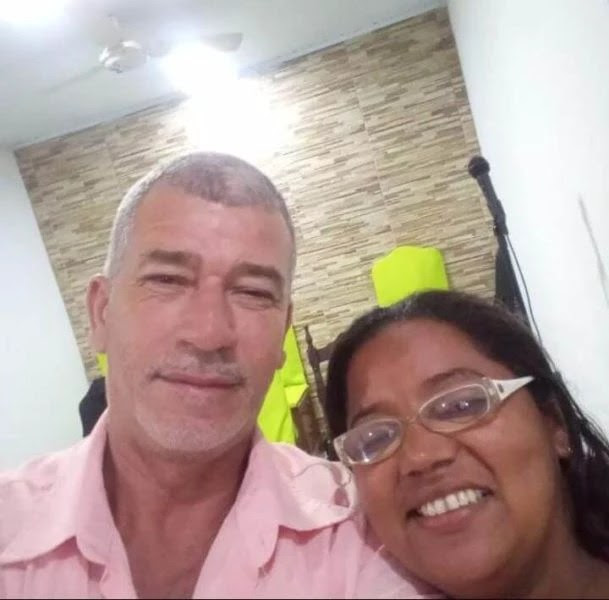 Carlos Roberto (à esq) e esposa Gisleide Carvalho (à dir). Carlos é um homem branco de cabelos grisalhos vestindo uma camisa rosa. Já sua esposa é uma mulher negra, que sorri para a foto e usa óculos de armação branca. Carlos foi preso por um crime que não cometeu.