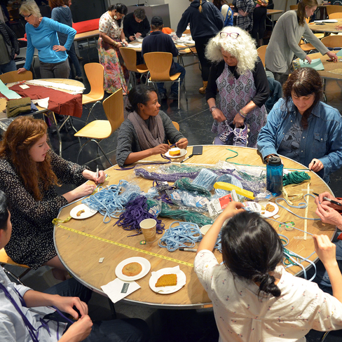 A group of people sit at a table sewing