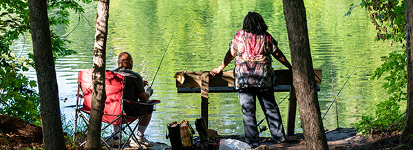 man with fishing rod and woman on wooded river bank