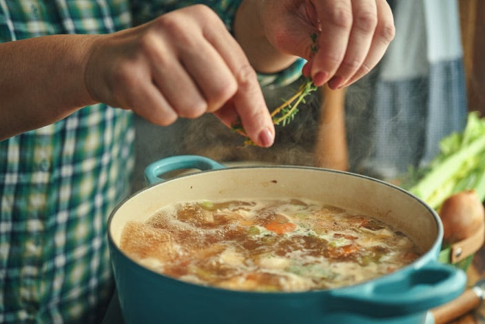 Close-up of someone making chicken soup from scratch in a large teal soup pot.