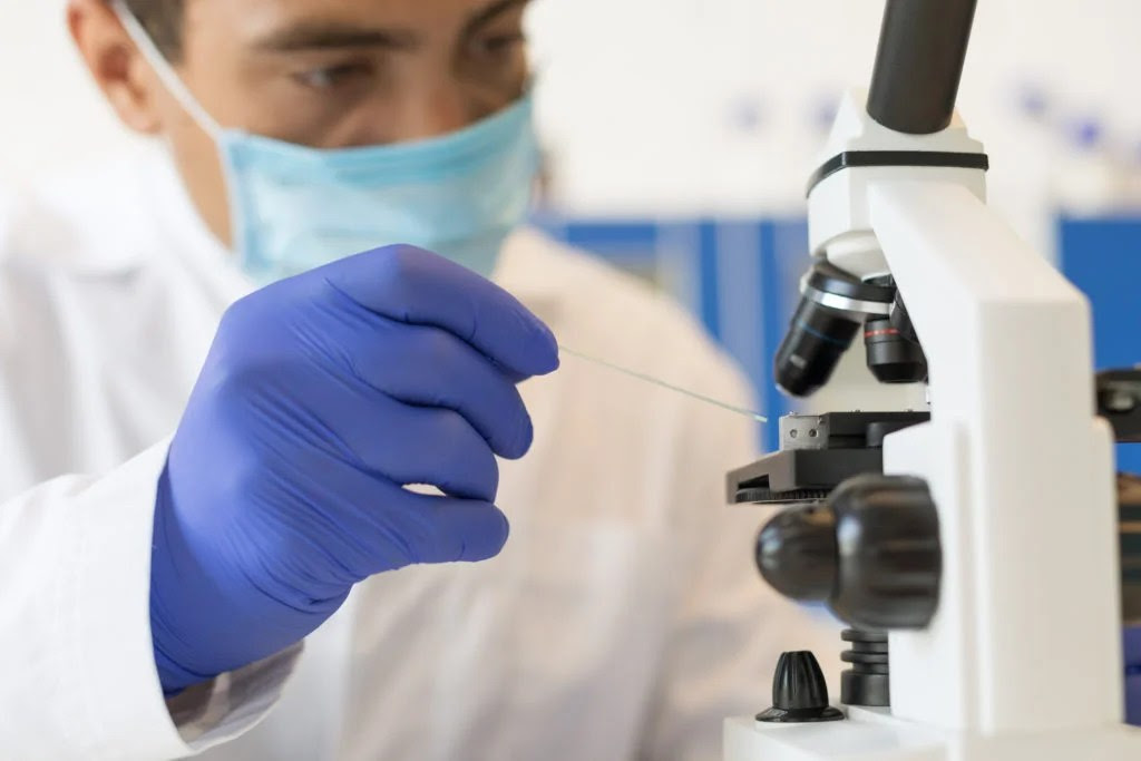 scientist wearing face mask working with microscope