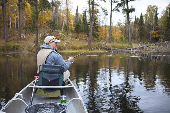 40s caucasian fisherman fishing from a canoe on small lake during fall