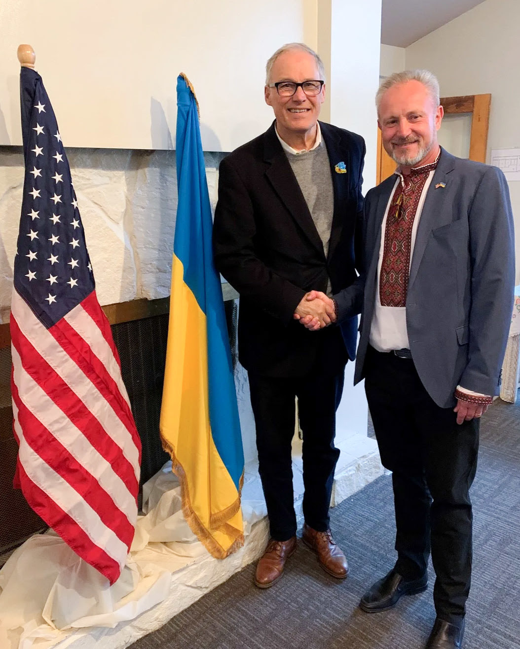 Gov. Jay Inslee shakes hands with a man standing in front of the American and Ukrainian flags.