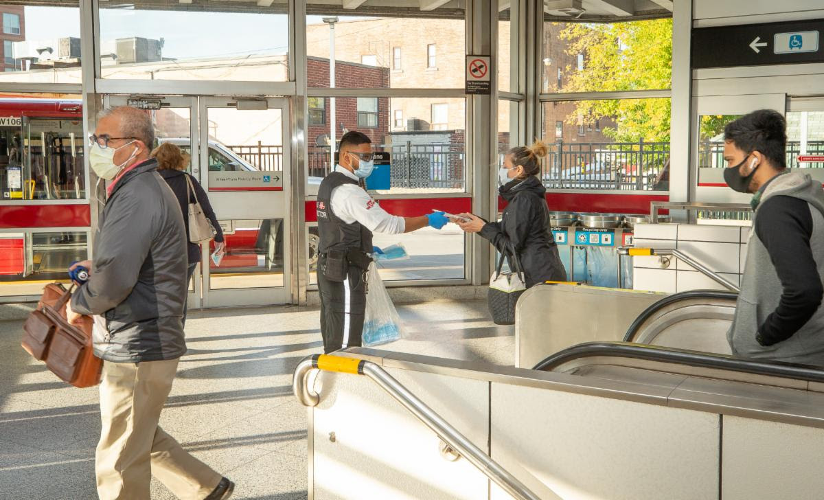 A TTC employee distributes masks to customers at Coxwell Subway Station