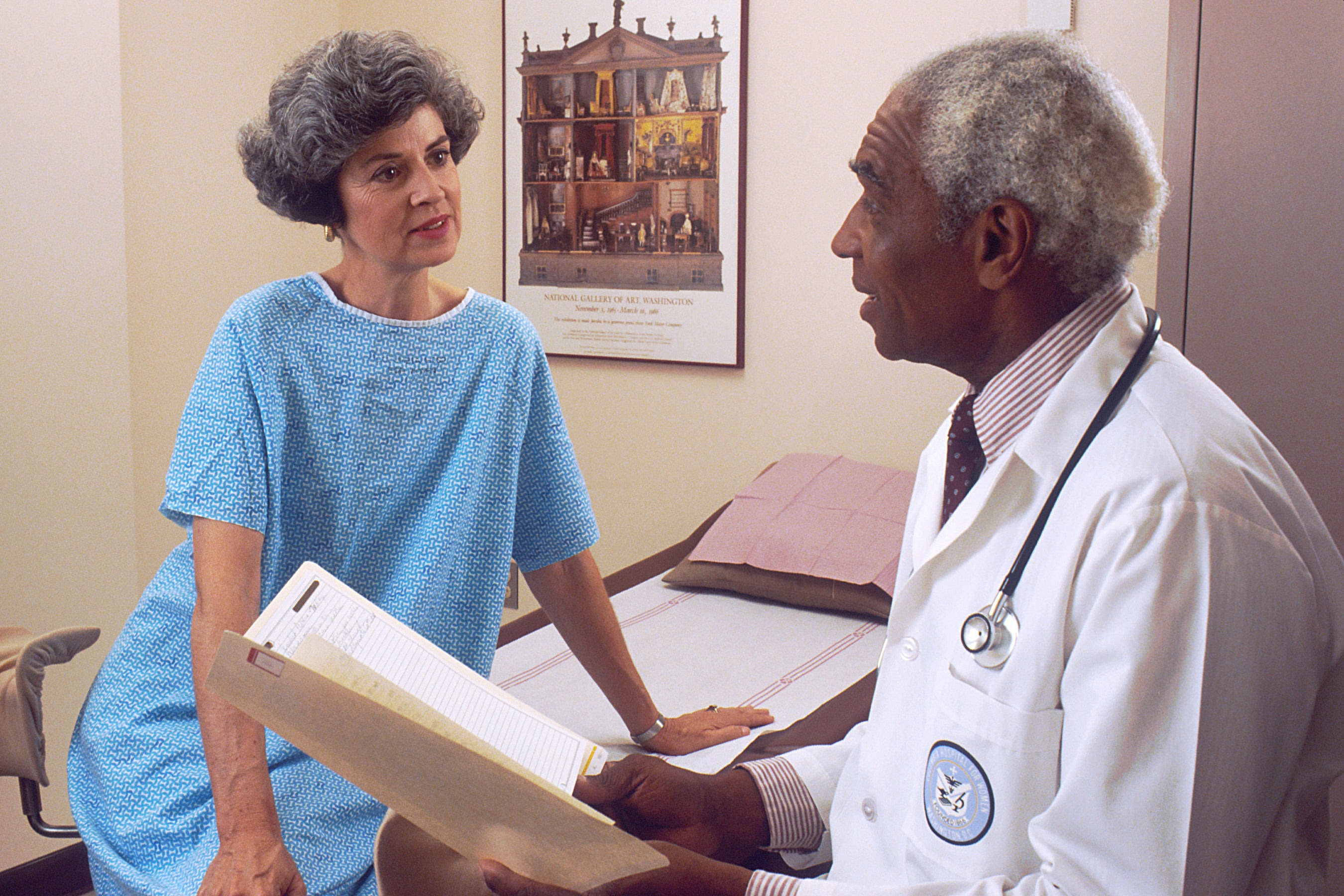 A black older male doctor consults with a white female patient in a hospital room, which should be standard in clinical trials.