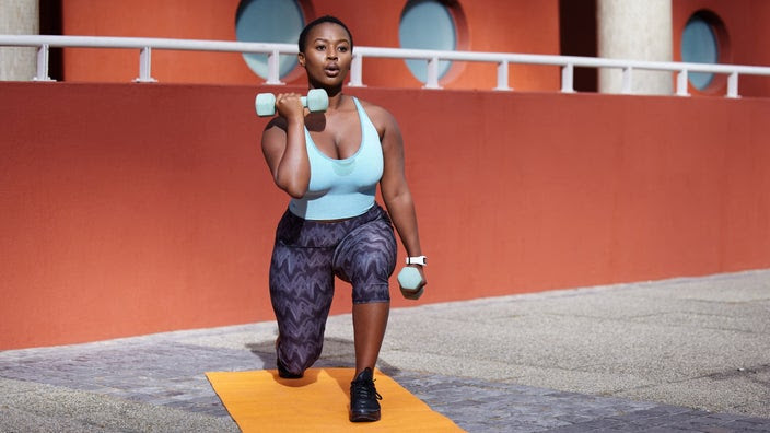 A person lifting dumbbells outside on a yoga mat.