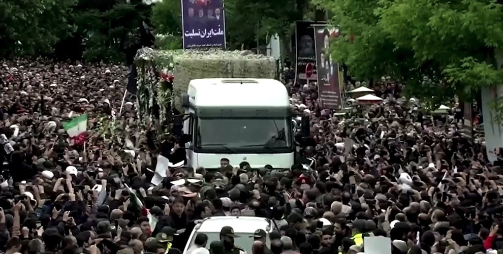 A large truck flanked on either side by a sea of people, Iranian flags in the crowd