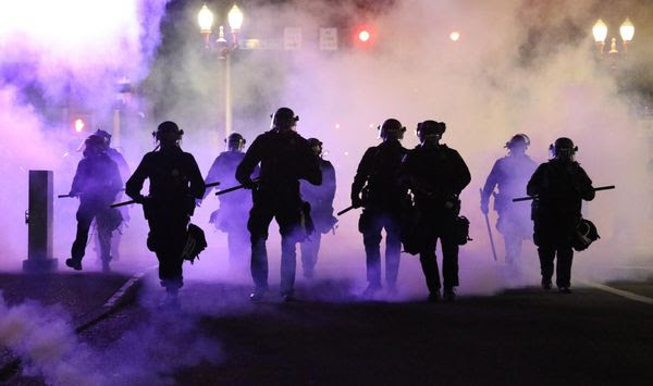 Police officers walk enveloped by teargas in Portland, Friday, March 29, 2020. After hours of largely peaceful demonstrations, violence escalated late Friday in downtown Portland, as hundreds of people gathered to protest the Minneapolis police killing of a black man, George Floyd . (Dave Killen/The Oregonian via AP)