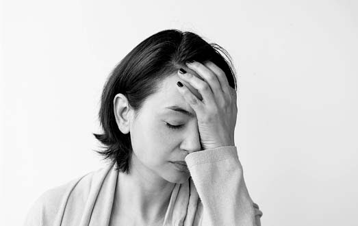 Portrait of a woman holding her hand on her forehead with her eyes closed.