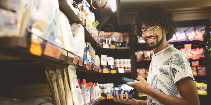 A young man in a grocery store 
smiles as he peruses the plant-based refrigerated section.