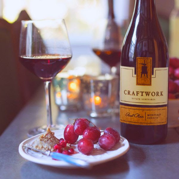 Bottle of Craftwork Estate Pinot Noir 2018 on a table with a glass of wine and a plate of grapes.