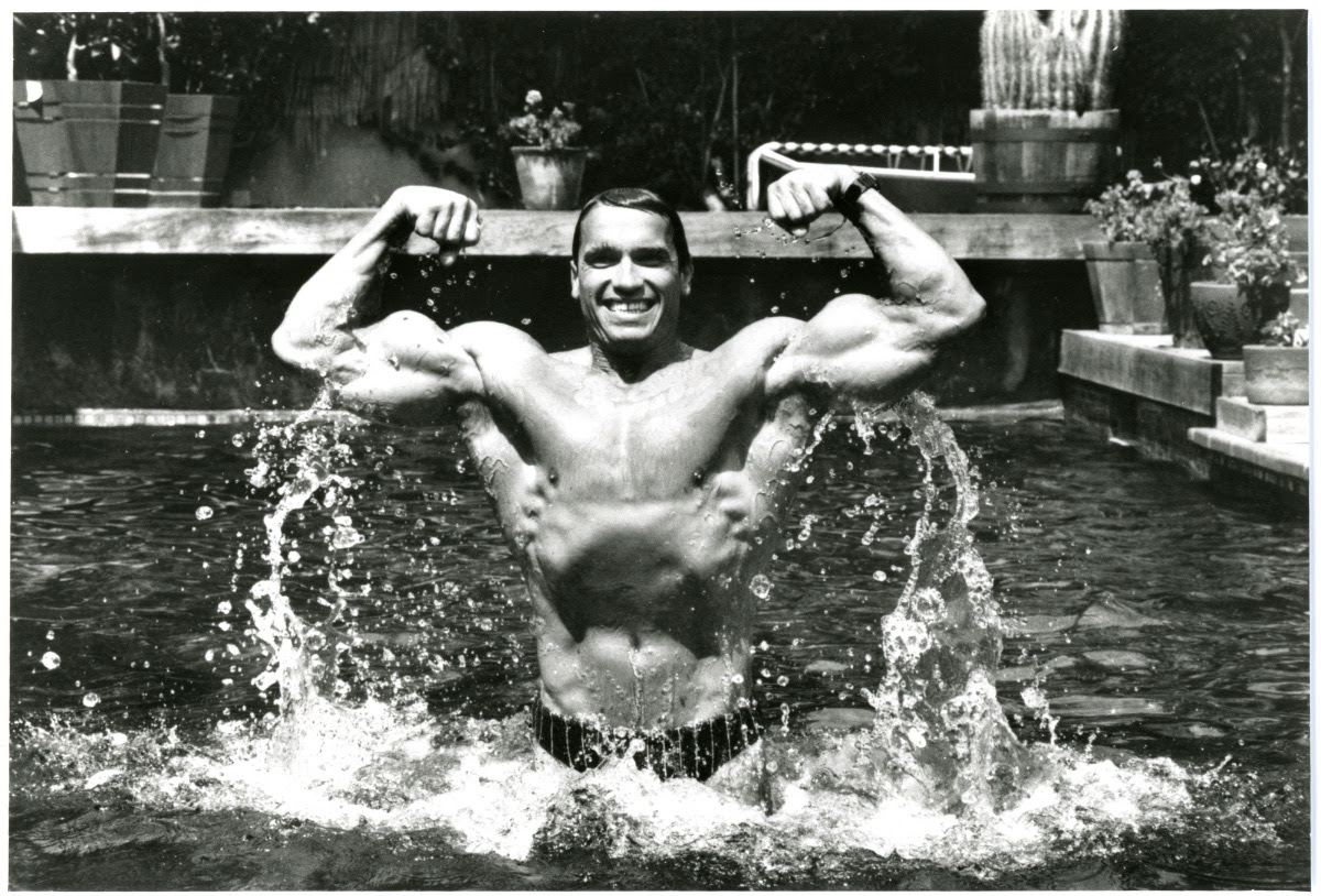 Arnold Schwarzenegger flexes as he rises out of a swimming pool