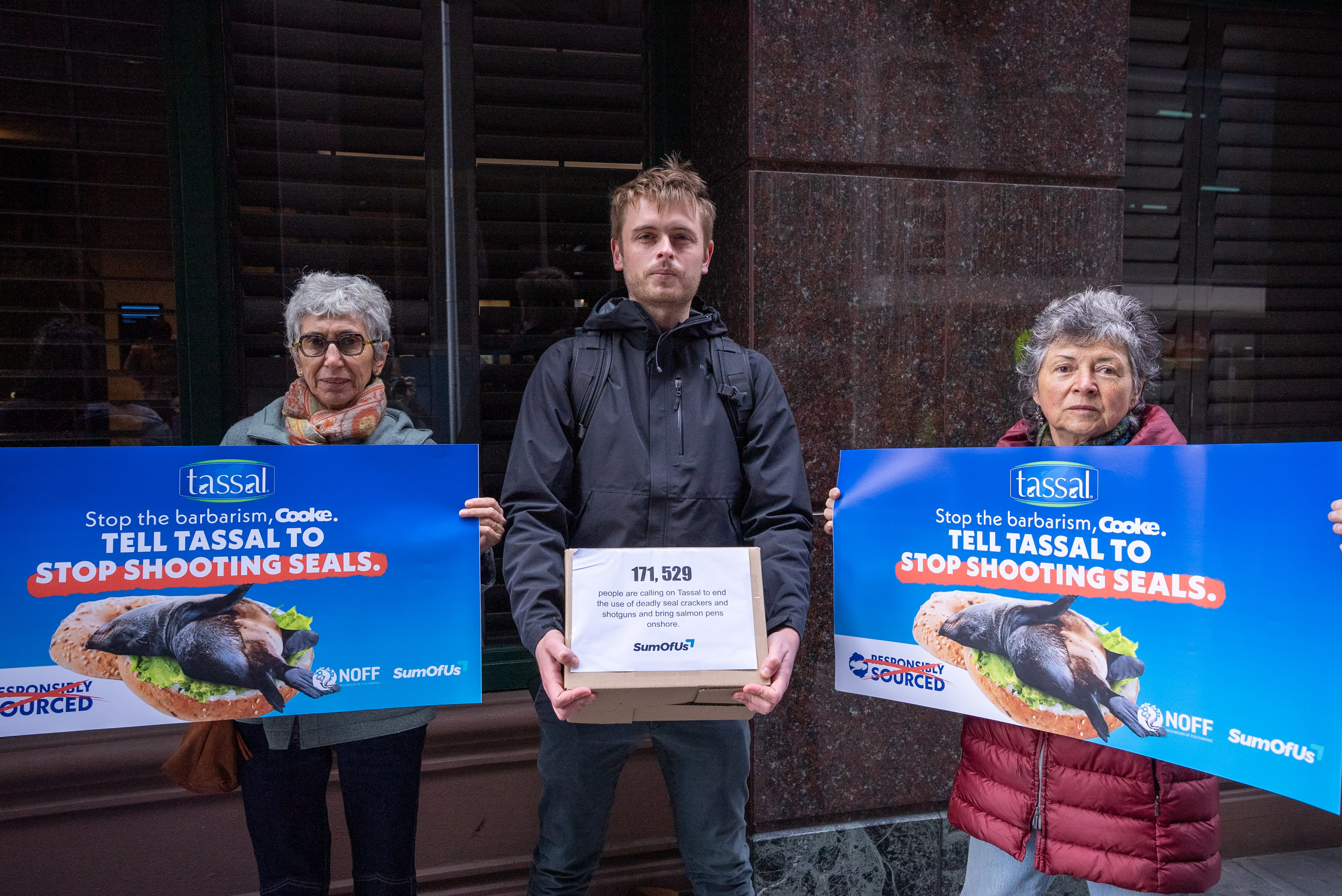 Man holds a petition box, two women hold signs.