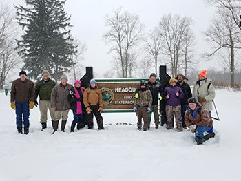 Group of stewardship volunteers in front of Fort Custer sign in winter
