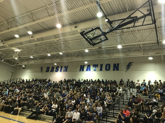 Students sit in the bleachers at Thunder Basin High School's gym during the dedication ceremony for the school. The words "BASIN NATION" are written in blue on the wall above where they are sitting with thunderbolts painted on each side representing the new schools' mascot.