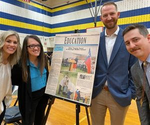 Alumni standing around news poster.