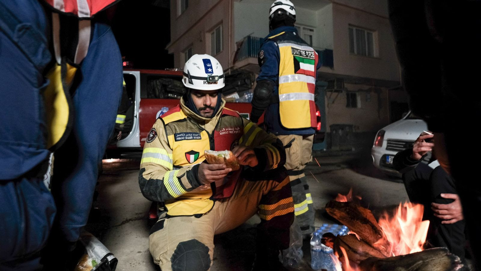 Emergency response worker eating a sandwich at night near a fire for warmth.