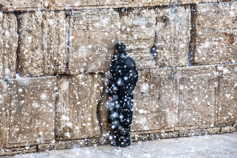 man praying at the western wall in jerusalem during a snow storm
