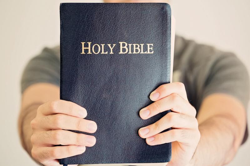 Close up of a young man proudly holding out his Bible