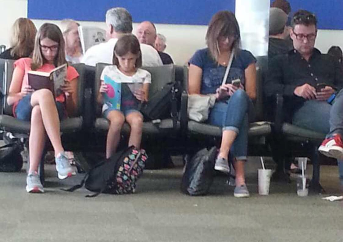 Poignant photo of kids reading books while parents are on cell phones
