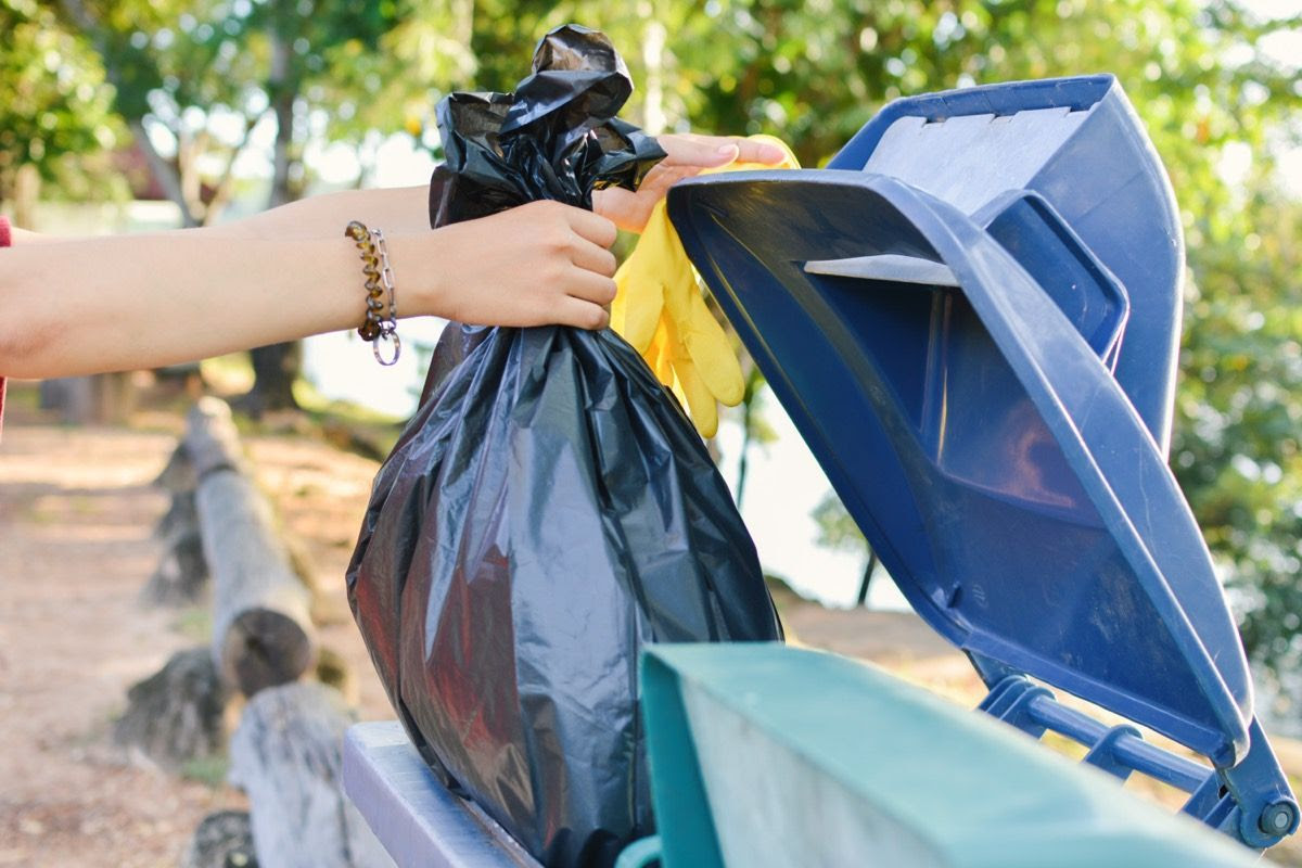 person throwing away black bag of trash