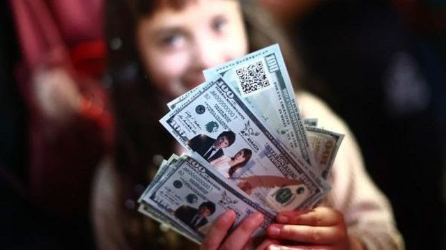 Menina segurando papeis que representam notas de dólar com o rosto de Milei e de sua vice-presidente