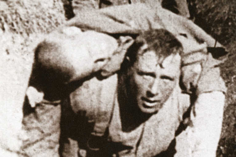 Black and white photo of a man carrying another man on his back.