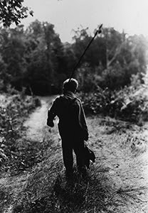 Historical photo of boy walking on trail carrying a fishing pole