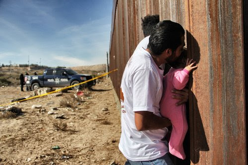 A man holds a baby up to the border wall between Mexico and United States. Photo Credit: HERIKA MARTINEZ/AFP/Getty Images.