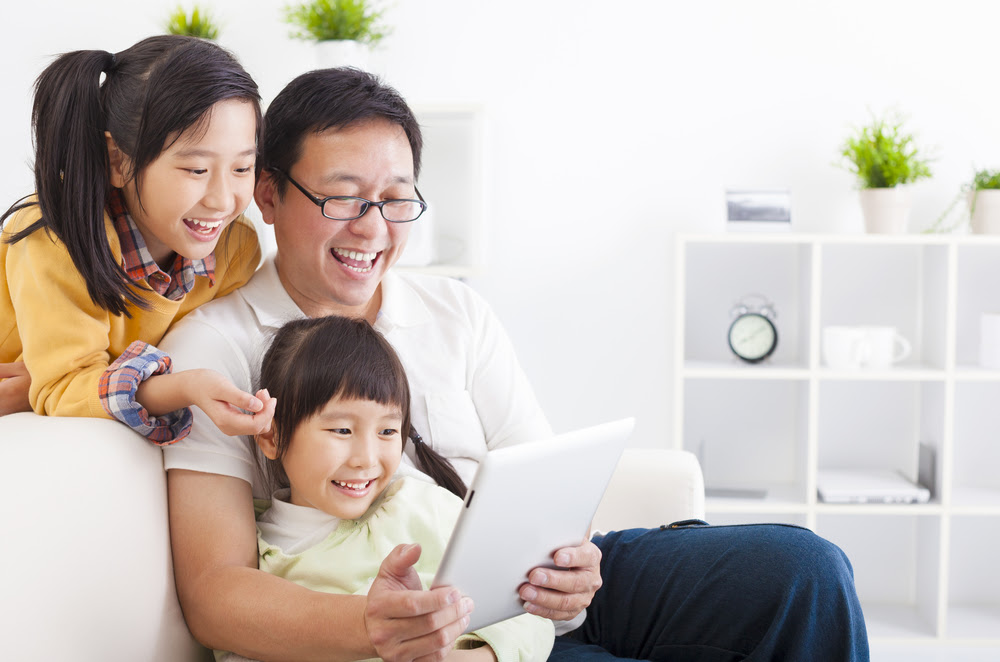 a Chinese father and two daughters looking at a tablet and laughing