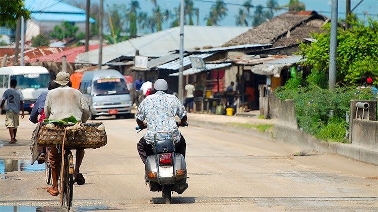 The figure shows two men riding along a busy street in Zanzibar, Tanzania