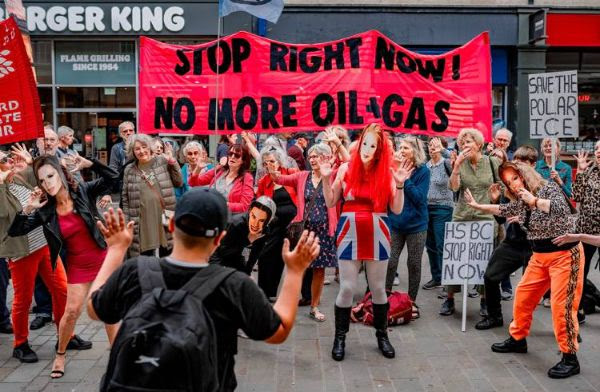 A group of people on a high street, with a large banner that says Stop right now! No more oil and gas