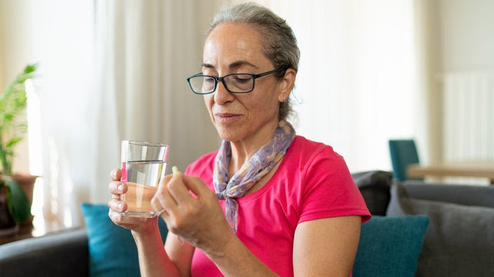 Woman taking pill with a glass of water.